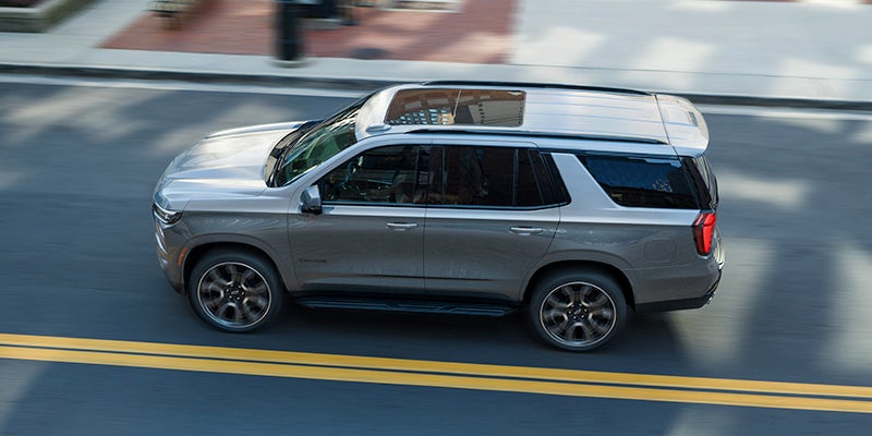 Side View of the 2025 Chevrolet Tahoe SUV Driving on a Road Lined with Businesses