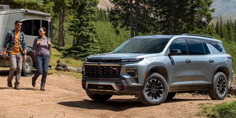 Three Quarters View of a Silver Chevy Traverse with a Man and a Woman Walking in Front of a Trailer