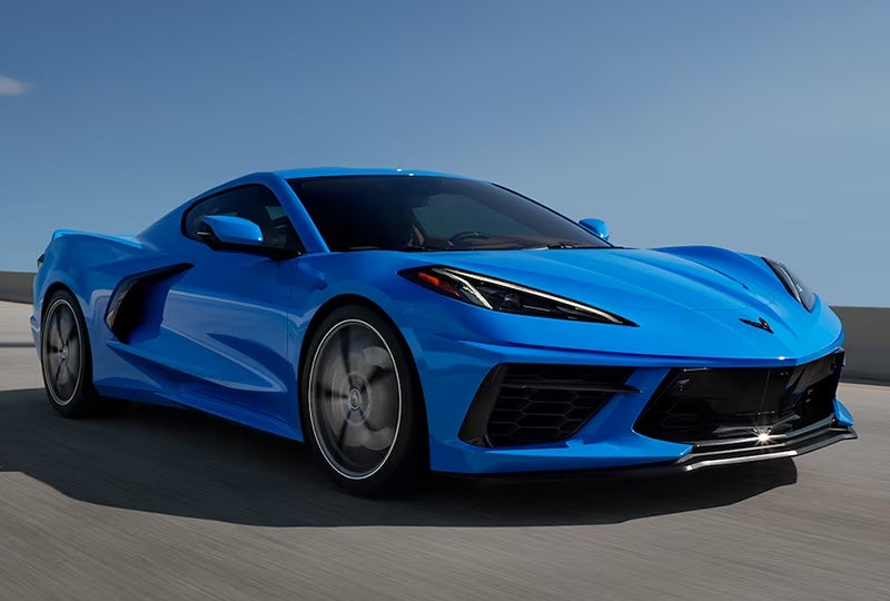 Side profile view of a 2024 Chevrolet Corvette in Rapid Blue driving over a bridge.