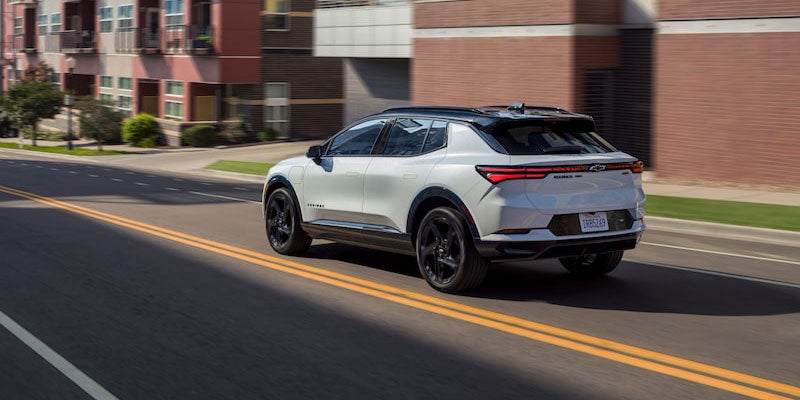 2024 Equinox EV 3RS in Summit White with Mosaic Black Metallic Roof Driving on a City Street