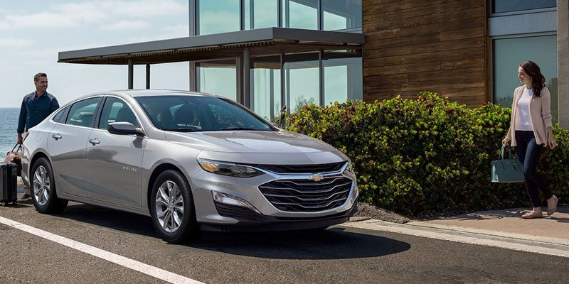 A Sterling Grey 2025 Chevy Malibu Parked in Front of a Home Under a Clear Blue Sky