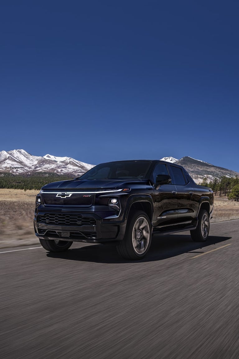 2024 Chevy Silverado EV Driving Down A Road With Mountains In The Background