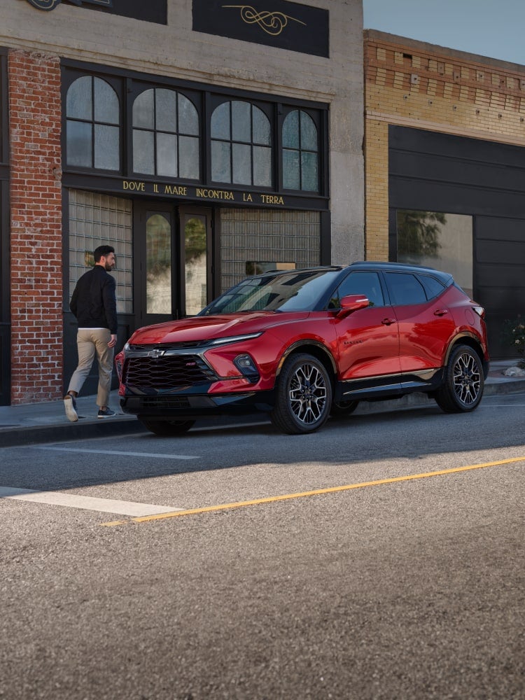 Man Walking Toward His 2025 Red Chevy Blazer Parked at a Shop