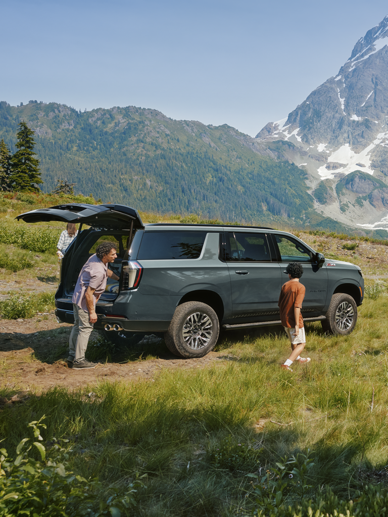 A family next to a 2025 Chevrolet Suburban with the rear lift gate opened in a mountainous field